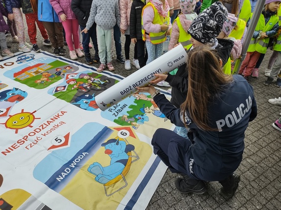 policjantka prezentuje tubę odblaskową na tle gry planszowej