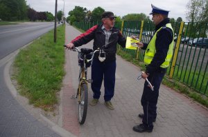 policjant wręcza rowerzystom odblaski i ulotki,  w tle droga i radiowóz policyjny
