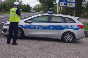 policjant mierzy prędkość pojazdu, w tle jadący samochód