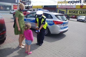 policjantka wręcza dziewczynce maskotkę, w tle parking
